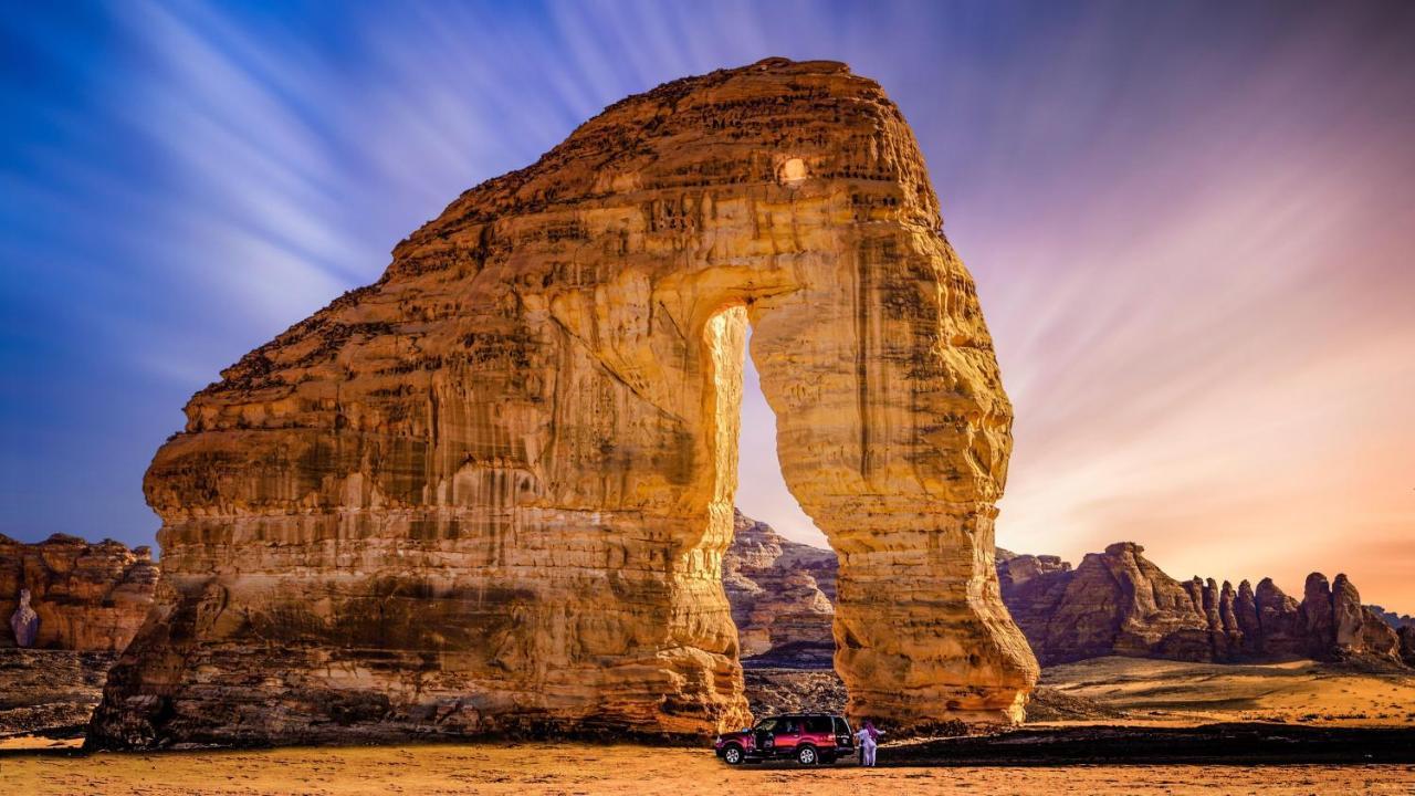 다르 알 이만 인터컨티넨탈 호텔 메디나 외부 사진 The photo depicts a striking rock formation, characterized by a large archway that has been sculpted by natural processes. The landscape around the formation features sandy terrain and rugged terrain, typical of desert environments. In the foreground