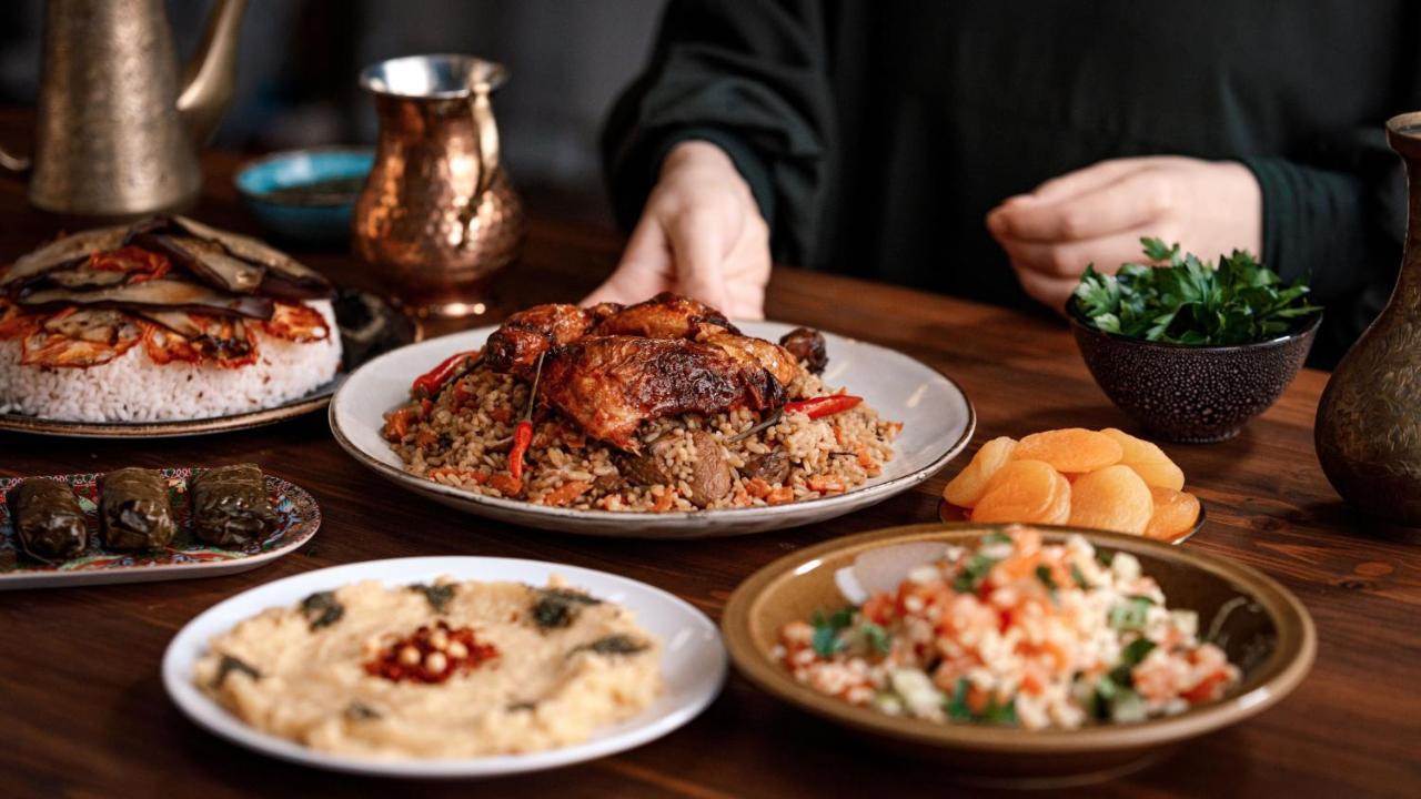 다르 알 이만 인터컨티넨탈 호텔 메디나 외부 사진 The photo displays a table set with an assortment of dishes. In the center, there is a large plate of pilaf or rice with pieces of roasted chicken, garnished with red peppers. Surrounding it are several smaller dishes:

1. A bowl of creamy dip or spr