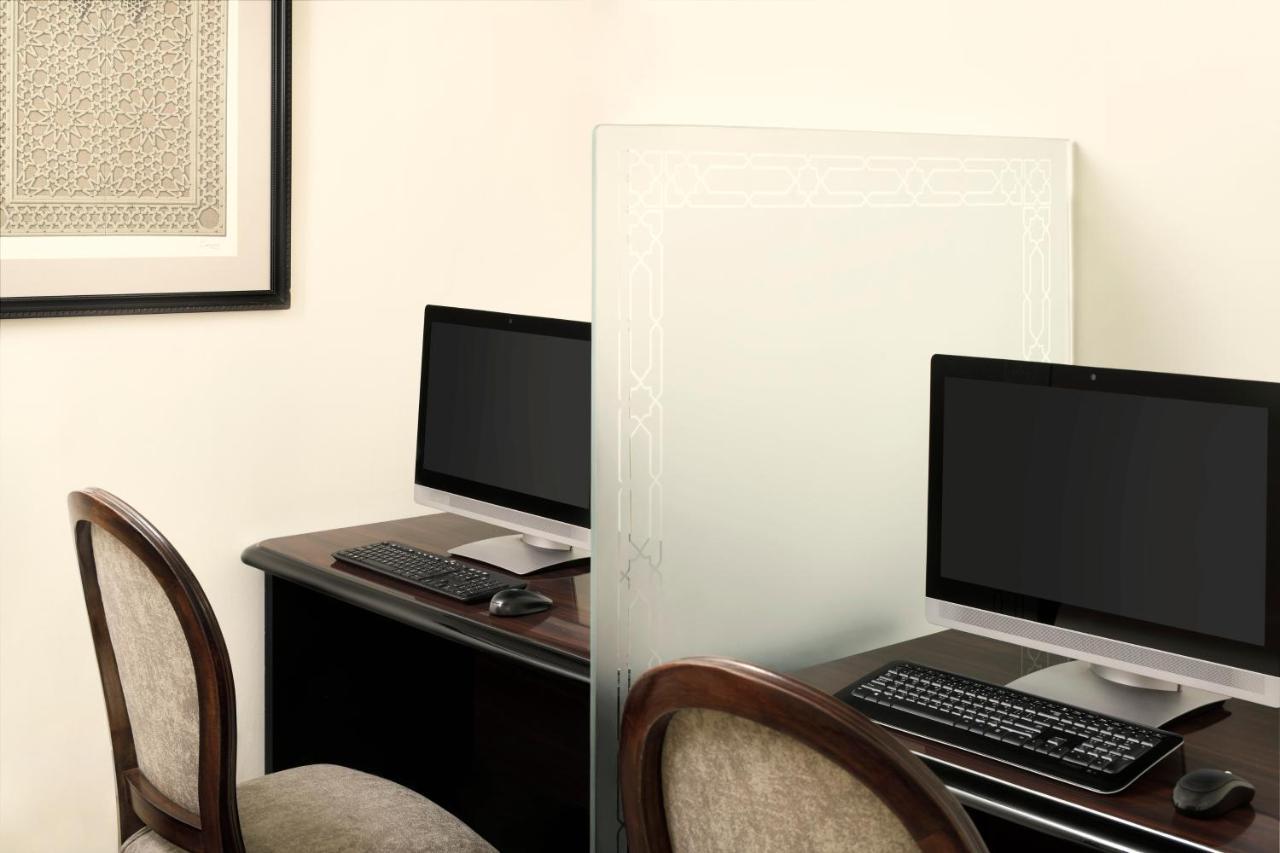 다르 알 이만 인터컨티넨탈 호텔 메디나 외부 사진 The photo shows a workspace featuring two computers set up on a dark wooden desk. Each computer has a monitor and a keyboard. A frosted glass partition is placed between the two workstations, providing some privacy. In the background, there is a fram