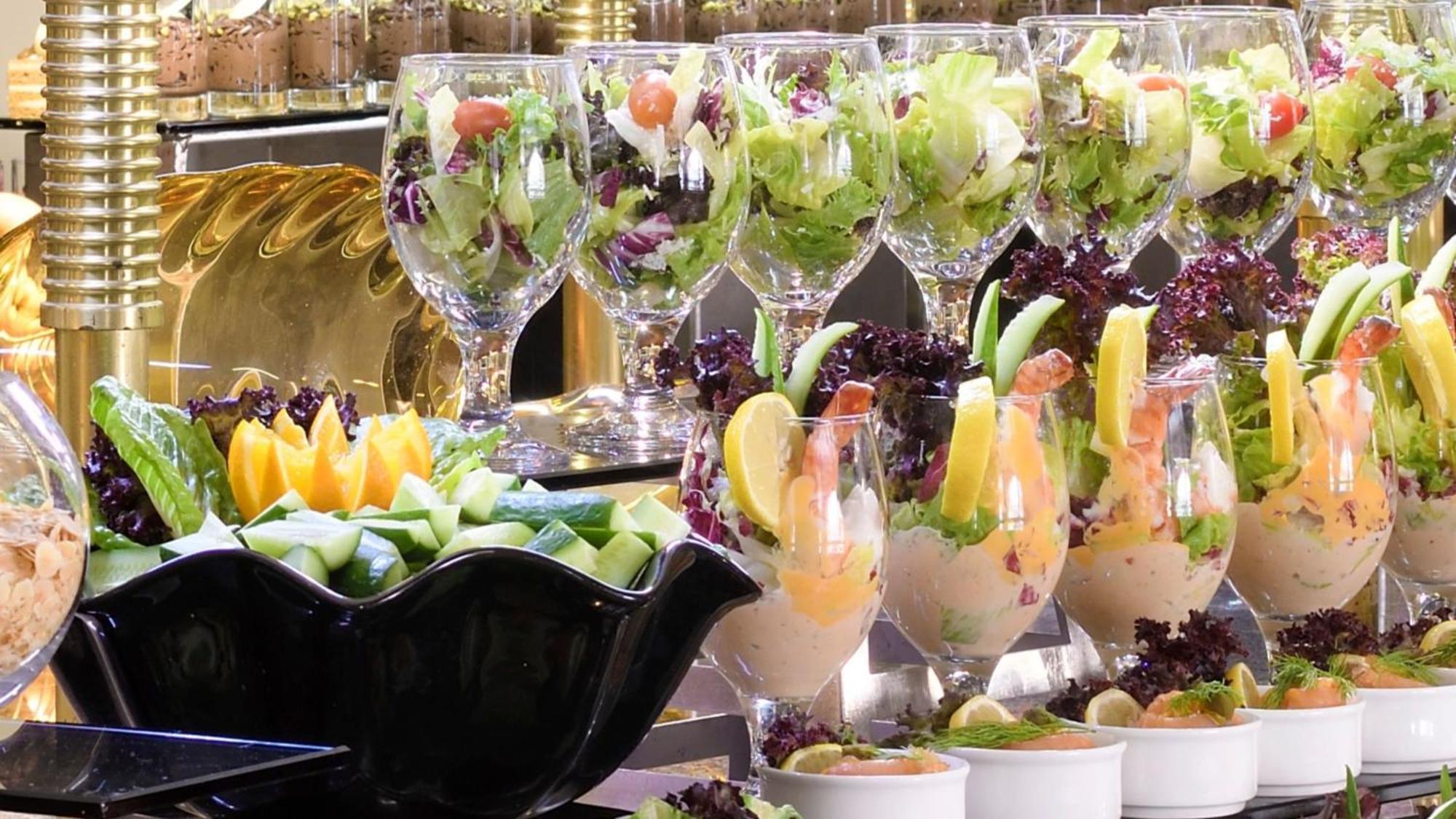 다르 알 이만 인터컨티넨탈 호텔 메디나 외부 사진 The photo features an elegant display of food items. In the background, there are several clear glasses filled with vibrant salads, featuring various types of greens and garnishes. In the foreground, there is a decorative black bowl containing cut pi