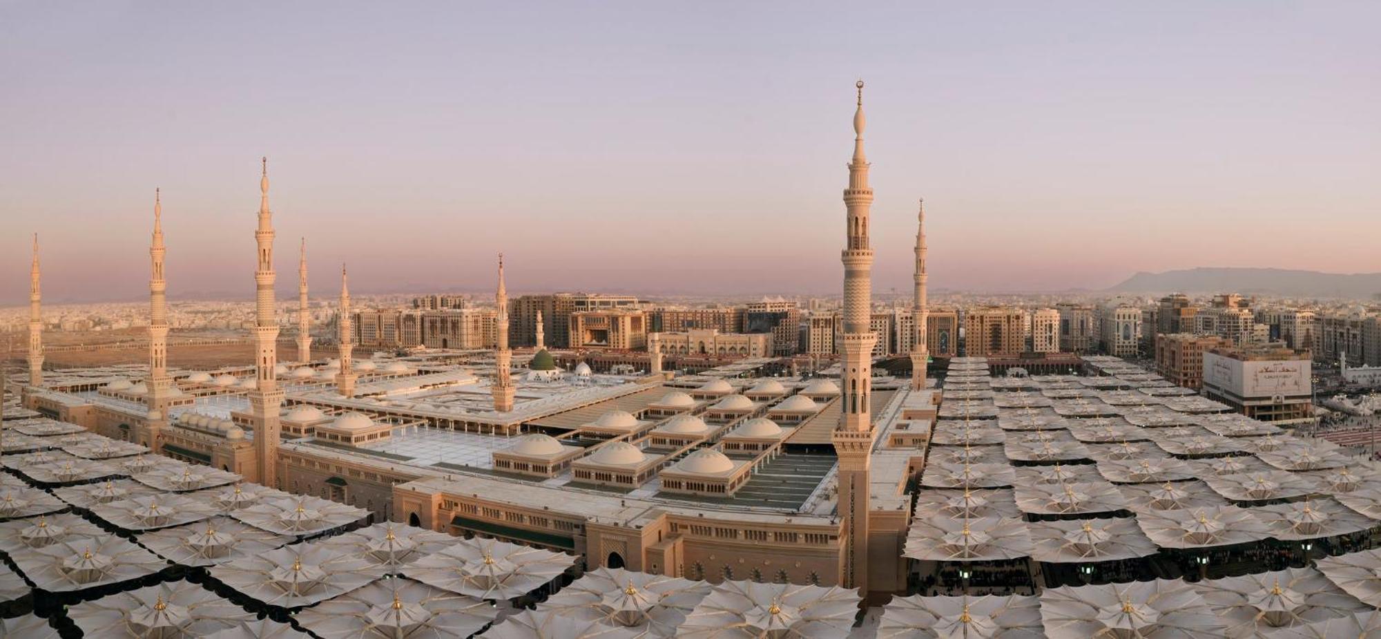 다르 알 이만 인터컨티넨탈 호텔 메디나 외부 사진 The photo shows an aerial view of the Al-Masjid an-Nabawi, or the Prophet's Mosque, located in Medina, Saudi Arabia. The mosque features distinct minarets, large white domes, and expansive open areas with large umbrellas that provide shade for visito