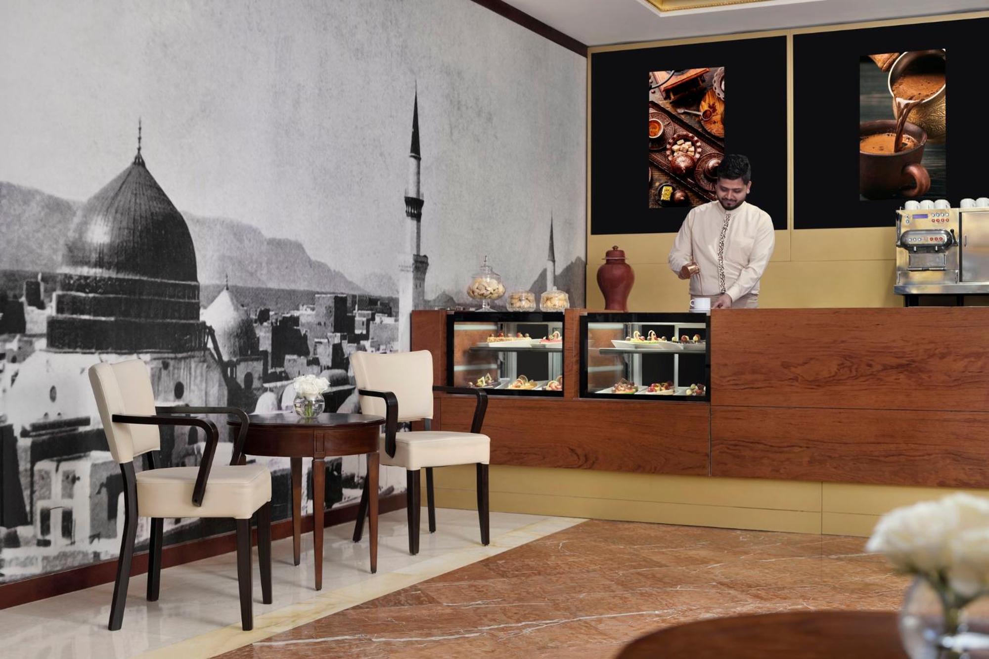 다르 알 이만 인터컨티넨탈 호텔 메디나 외부 사진 The photo shows a stylish interior of a café or pastry shop. In the background, there is a large black-and-white mural depicting a cityscape, featuring a prominent dome and minaret, suggesting an architectural style that could be from a Middle Easter