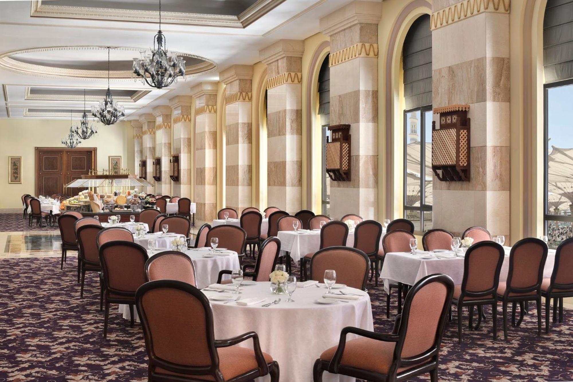 다르 알 이만 인터컨티넨탈 호텔 메디나 외부 사진 The photo depicts an elegant dining room setting. It features several round tables covered with white tablecloths, each set with dishes and glassware. The room has a sophisticated ambiance, characterized by high ceilings adorned with chandeliers and 