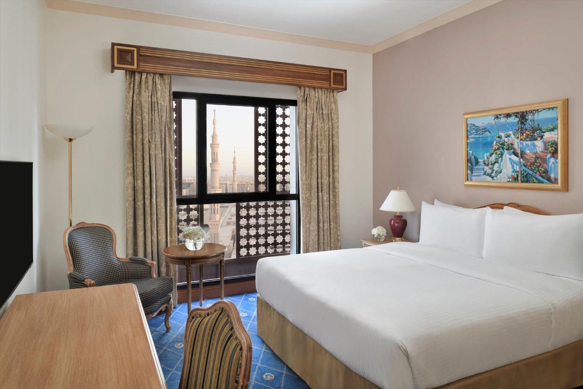 다르 알 이만 인터컨티넨탈 호텔 메디나 외부 사진 The photo shows a hotel room with a modern design. There is a large bed with white linens placed against the wall. Next to the bed, there is a small bedside table with a lamp. A comfortable armchair is situated nearby, accompanied by a wooden desk. T