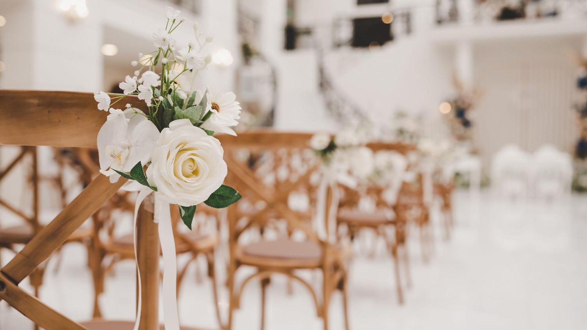 다르 알 이만 인터컨티넨탈 호텔 메디나 외부 사진 The photo showcases a beautifully arranged event space, likely set up for a wedding or special occasion. In the foreground, wooden chairs are neatly lined up, some adorned with decorative floral arrangements. The flowers include white roses and small