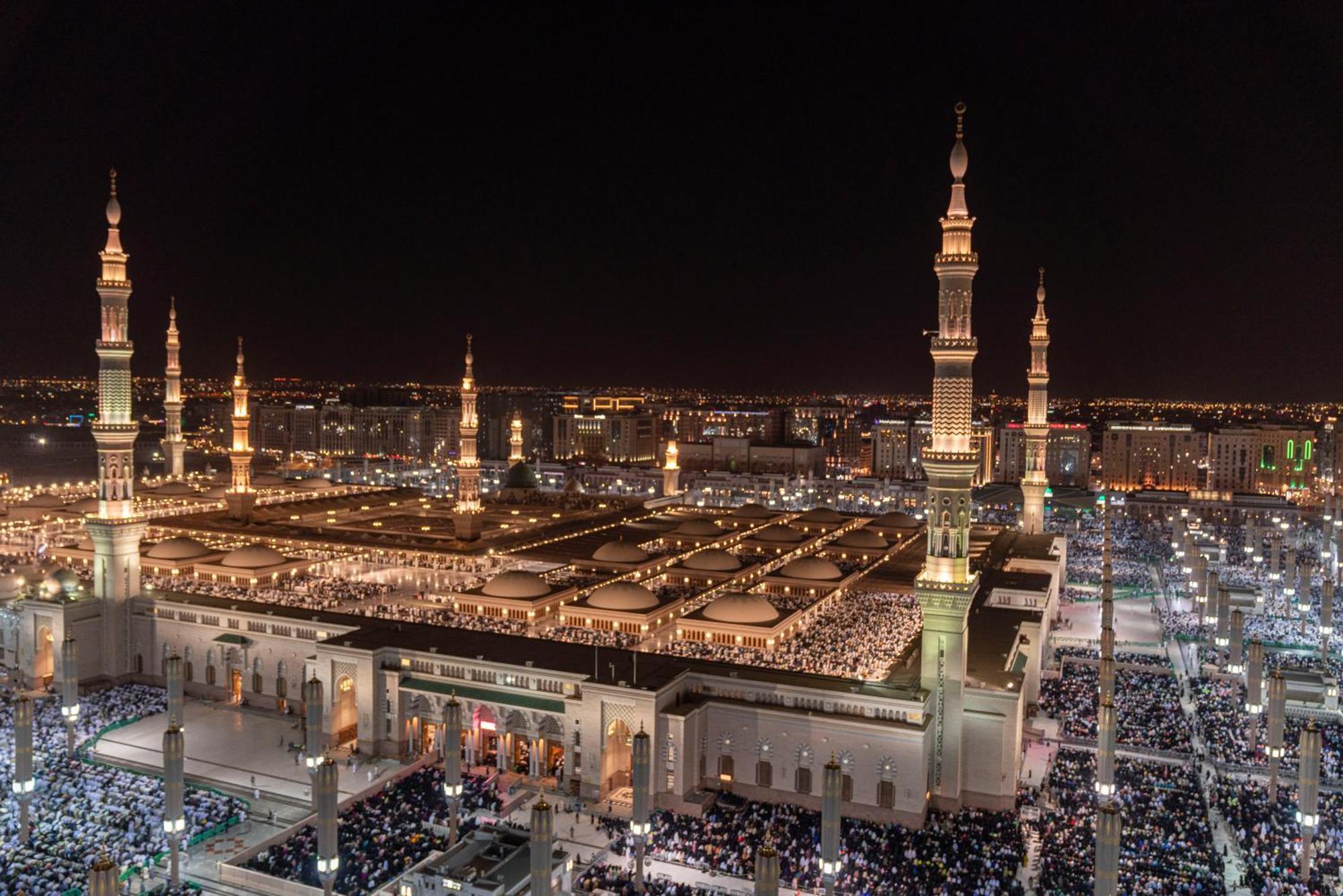 다르 알 이만 인터컨티넨탈 호텔 메디나 외부 사진 The photo shows a panoramic view of a large mosque complex illuminated at night. It features tall minarets with lights, a vast courtyard filled with people, and a beautifully lit architectural design. The overall ambiance suggests a significant space