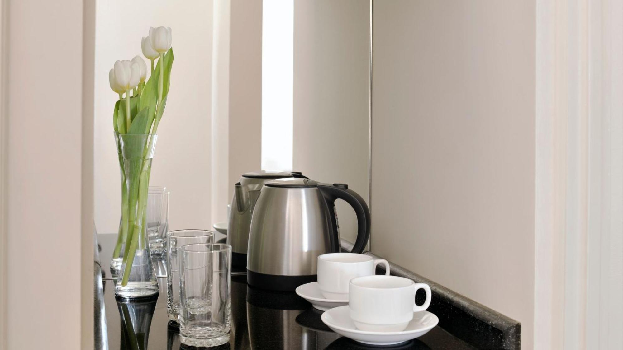 다르 알 이만 인터컨티넨탈 호텔 메디나 외부 사진 The photo depicts a neatly arranged beverage area. In the foreground, there are two white coffee cups on small saucers. Next to them, there are two clear drinking glasses. In the background, there is a silver electric kettle, which is positioned next