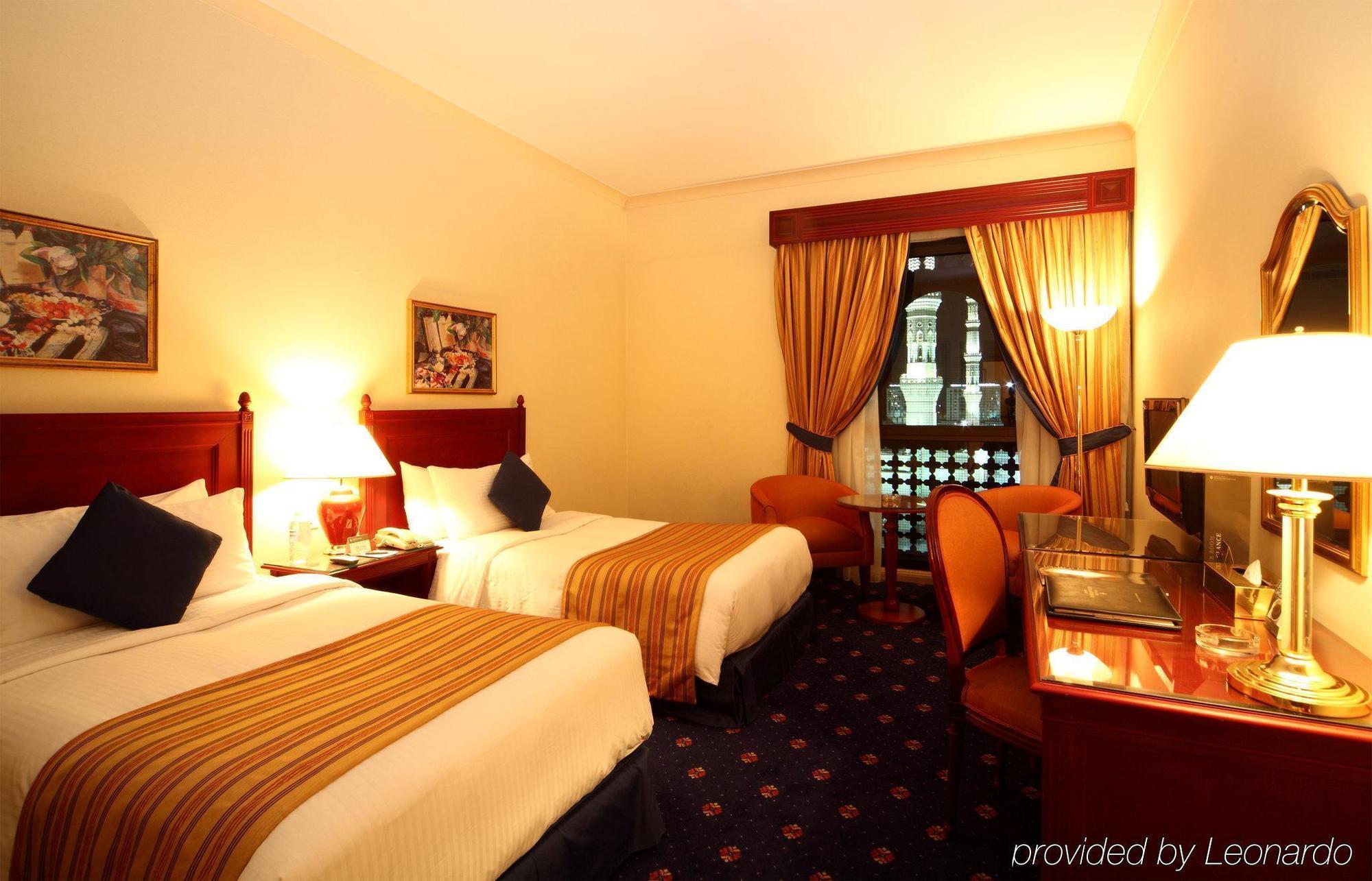 다르 알 이만 인터컨티넨탈 호텔 메디나 객실 사진 The photo shows a hotel room featuring two twin beds with white linens and brown striped bedspreads. There are decorative pillows on the beds, and the room has warm-colored walls. To the side, there's a small sitting area with a round table and a cha