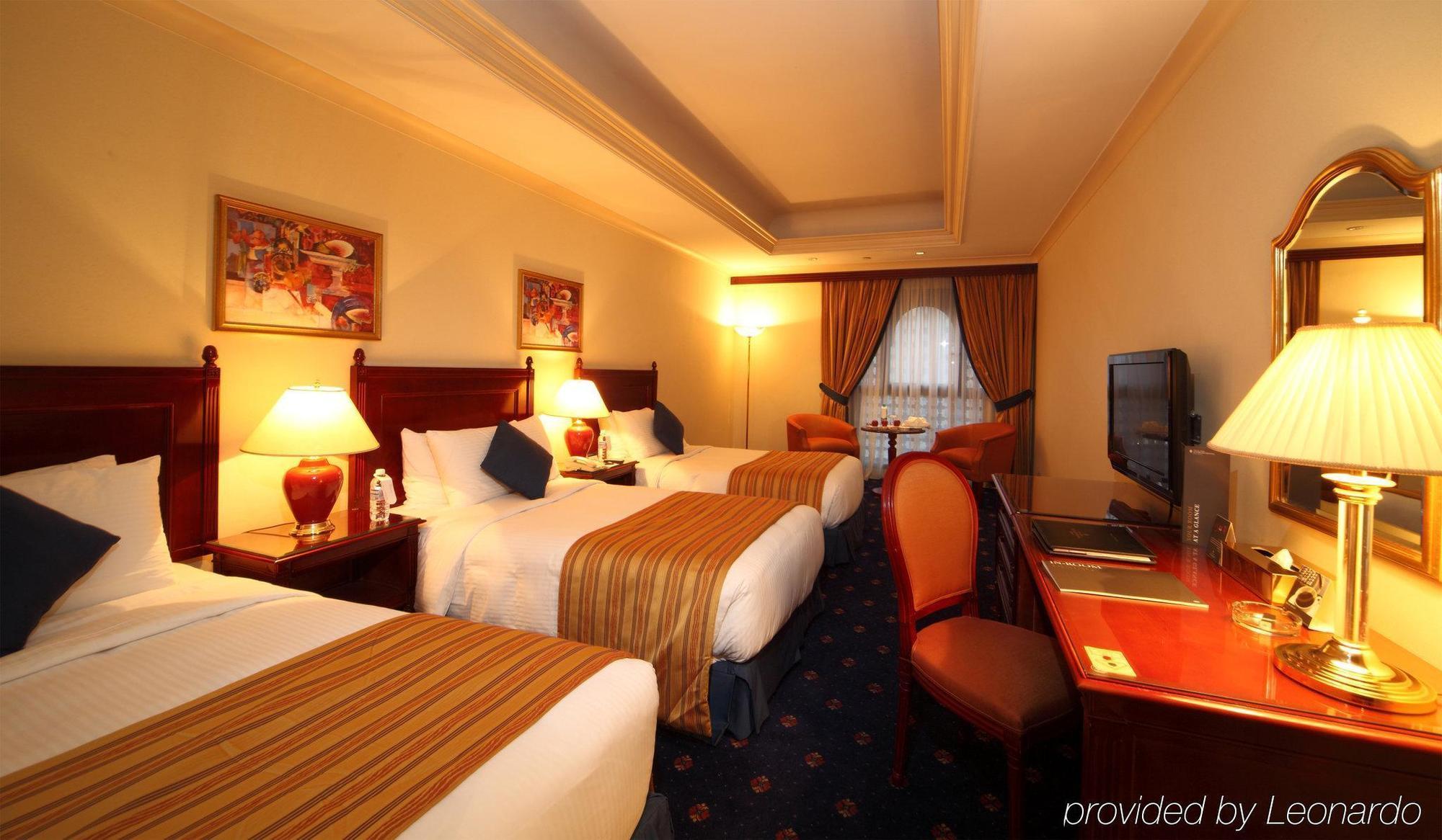 다르 알 이만 인터컨티넨탈 호텔 메디나 객실 사진 The photo shows a hotel room with a warm and inviting atmosphere. There are two beds with white and gold bedding, complemented by decorative pillows. Each bed has a bedside lamp. In the background, there's a small seating area with a couple of chairs