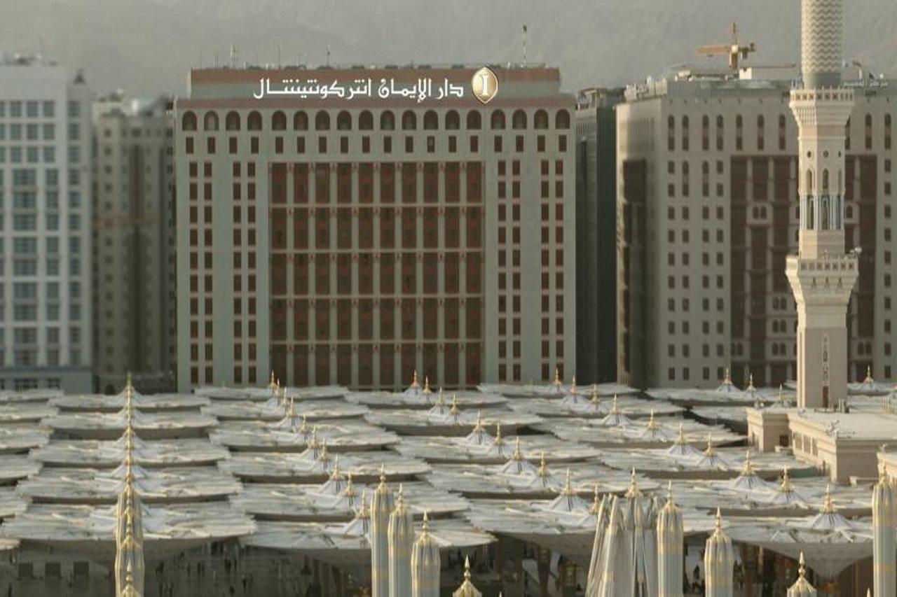 다르 알 이만 인터컨티넨탈 호텔 메디나 외부 사진 The photo shows a view of a large building with a modern architectural design, which appears to be a hotel or a commercial establishment. In front of the building, there are several large white canopies that provide shade, likely in a public space or